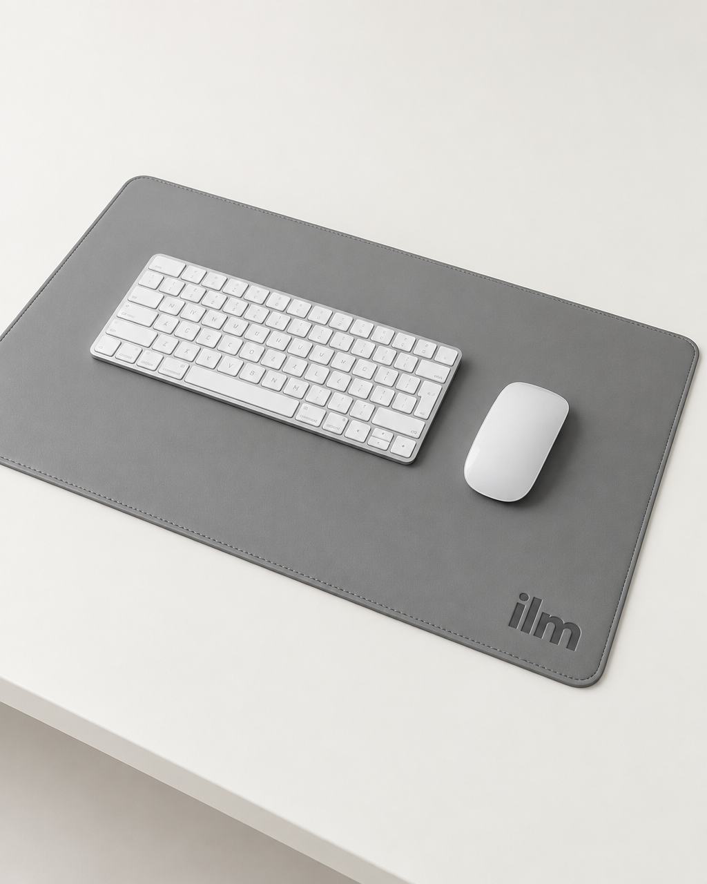 The grey ilm desk mat in use on a white desk, with a wireless keyboard and mouse
